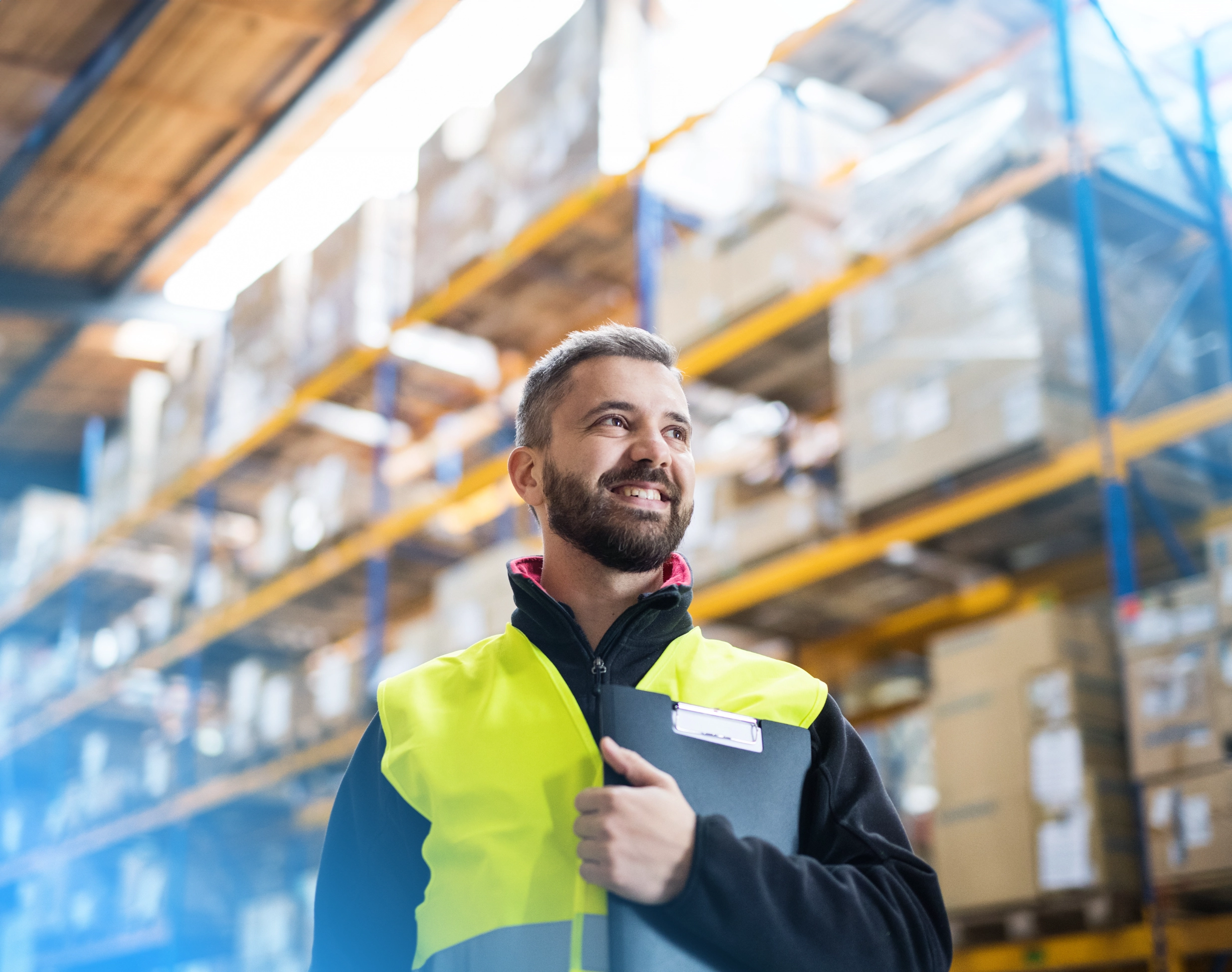 Smiling logistics worker holding a clipboard in a warehouse, ready to optimize the packing process with CloudConnect's advanced NetSuite solution.