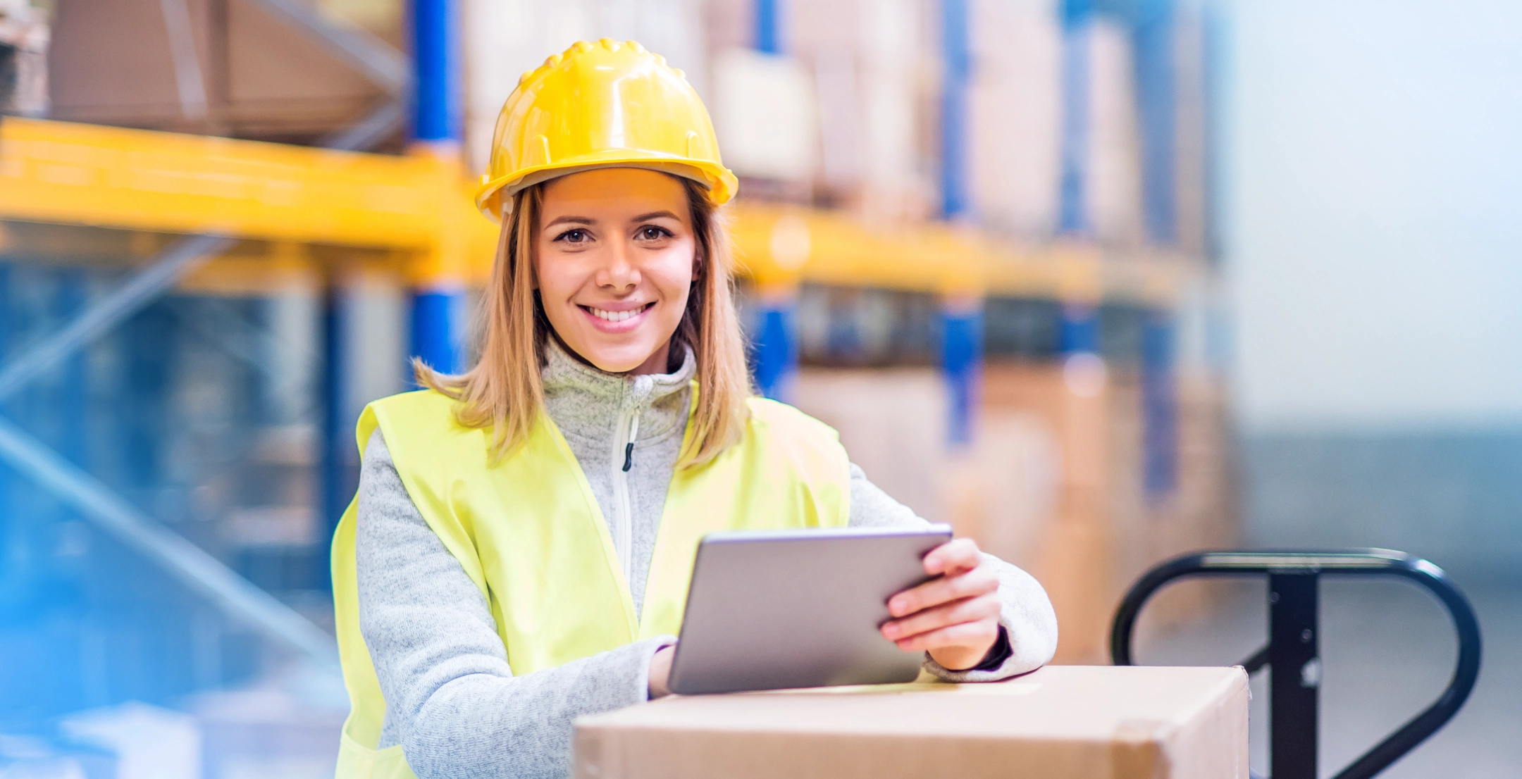 Logistics worker in warehouse smiling while using tablet.