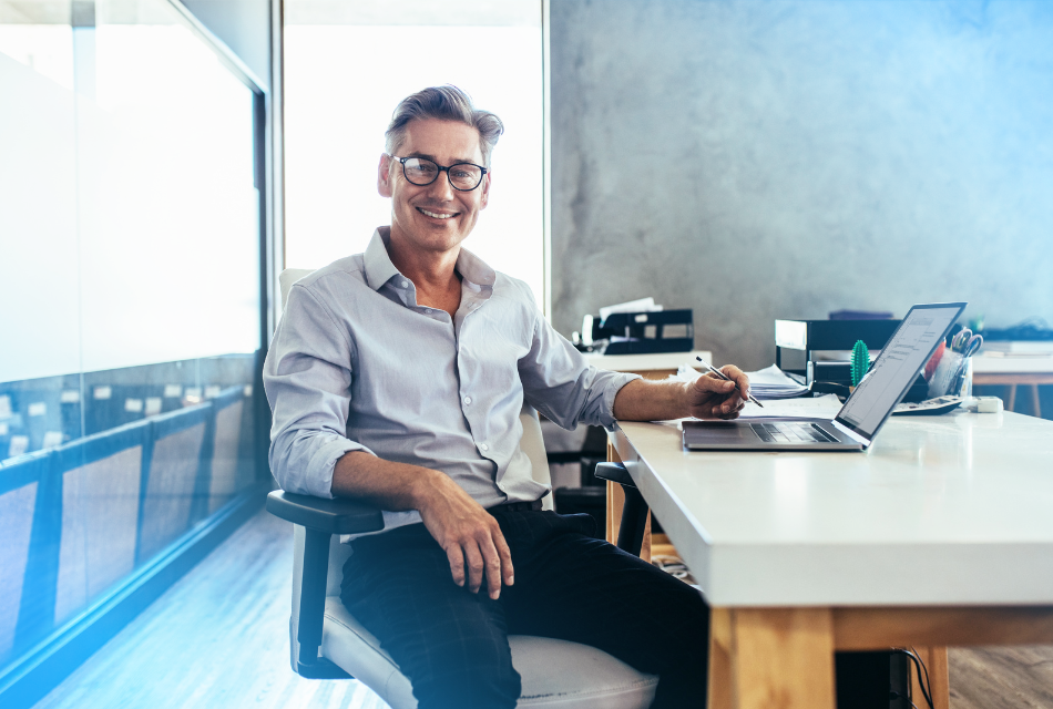 Smiling man at desk with laptop, representing ease and efficiency of CloudConnect's NetSuite AR Automation process.