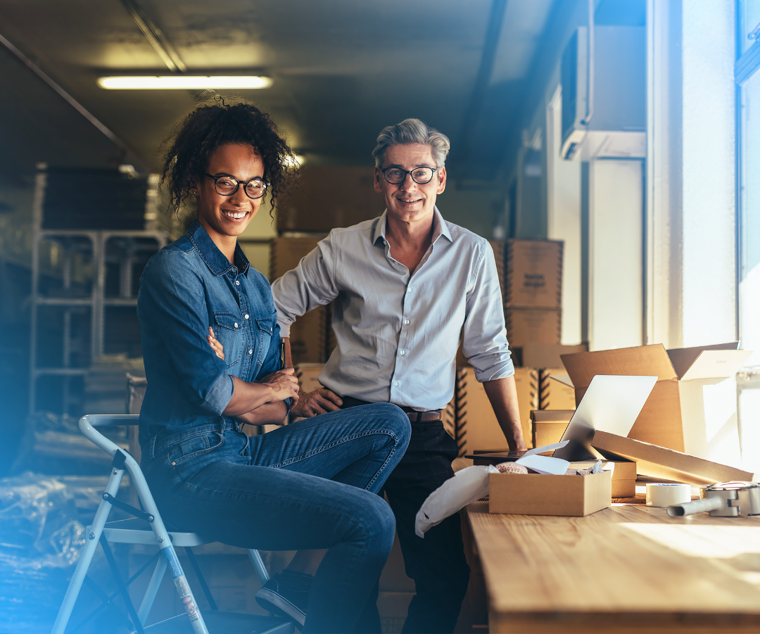 Two people smiling next to packages, illustrating the collaboration and success achieved through synchronized data between HubSpot and NetSuite.