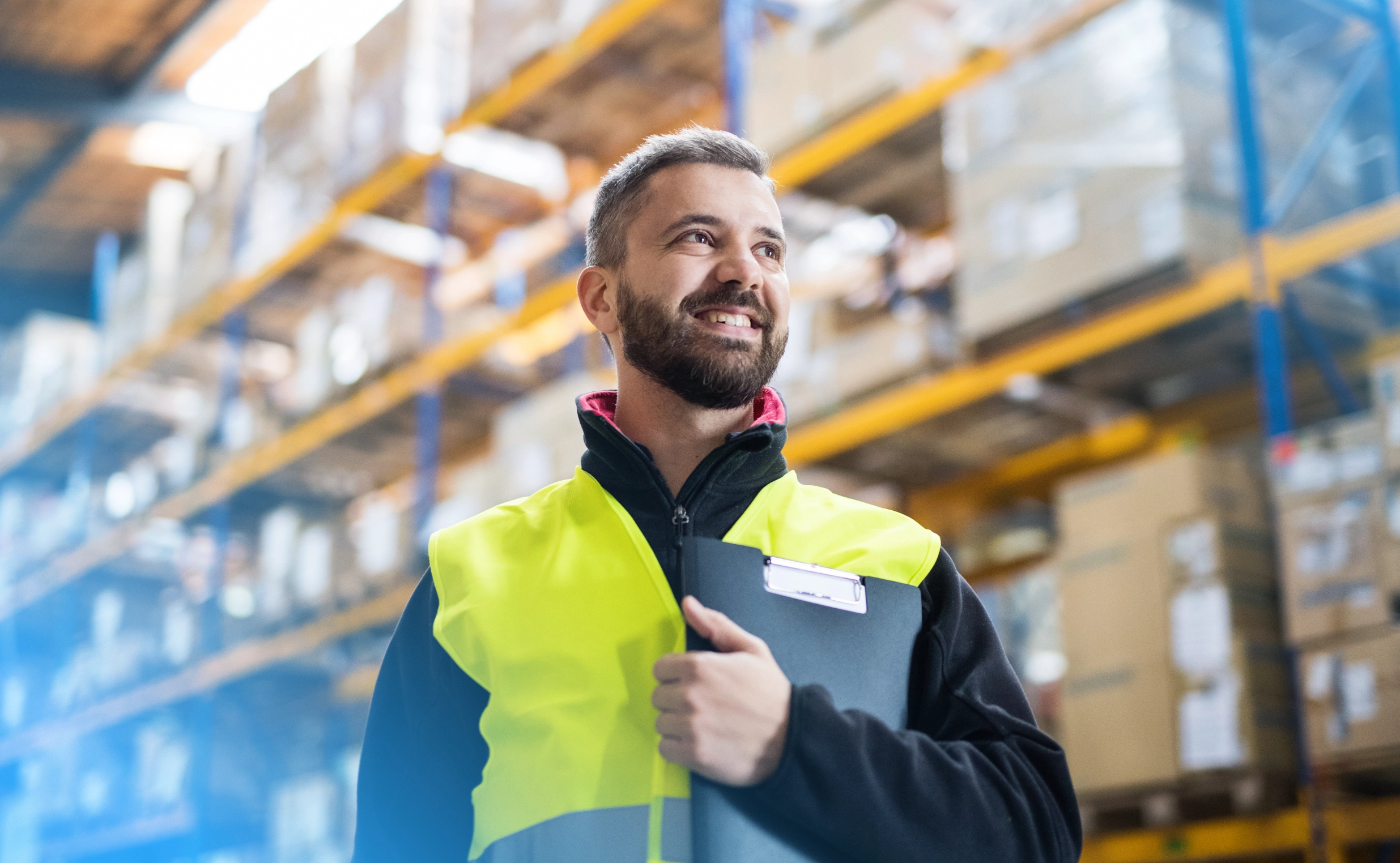 Smiling logistics worker holding a clipboard in a warehouse, ready to optimize the packing process with CloudConnect's advanced NetSuite solution.